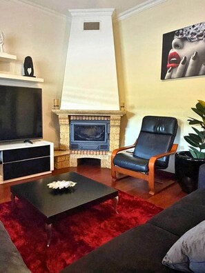 A living room with a fireplace, a black leather chair, a red rug, and a television. - Refúgio do Atalho by Stayguest (Santana)