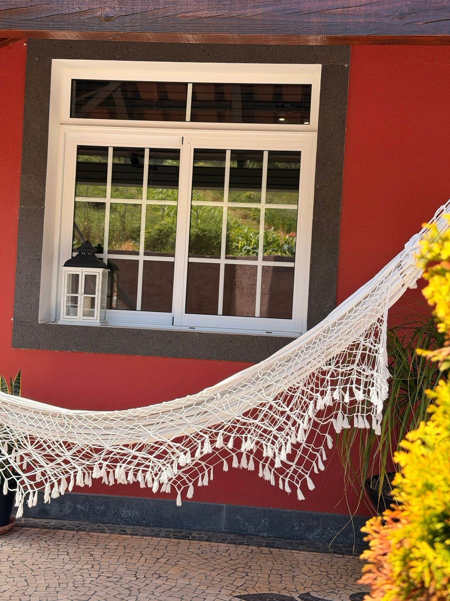 A hammock tied to a window with a view of greenery outside.