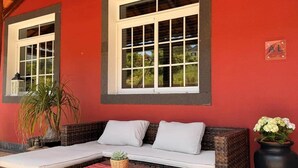 An outdoor seating area with wicker furniture, a red wall, and a window with a white frame. - Refúgio do Atalho by Stayguest (Santana)