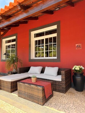 An outdoor seating area with wicker furniture, a red wall, and a window with a white frame. - Refúgio do Atalho by Stayguest (Santana)
