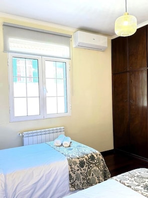 Ein Schlafzimmer mit Bett, Heizkörper, Fenster mit Rollläden, Klimaanlage und Kleiderschrank.