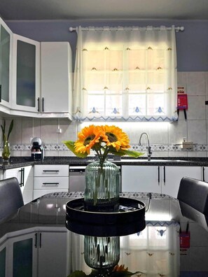 Eine moderne Küche mit weißen Schränken, einem Esstisch mit Glasplatte und einer Vase mit Sonnenblumen.