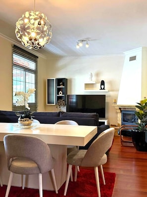 A modern living room with a dining area, a sofa set, a TV, and a fireplace. - Refúgio do Atalho by Stayguest (Santana)