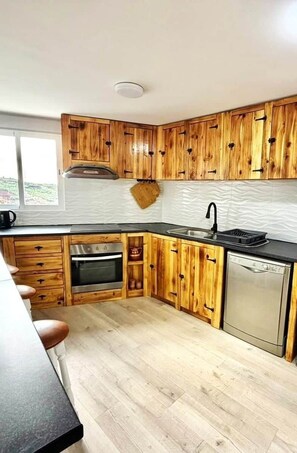 Eine Küche mit Holzausstattung, einem Edelstahlbackofen, einem Geschirrspüler und einem Fenster, das für natürliches Licht sorgt.
