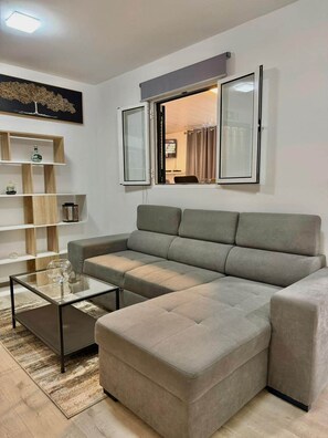 Ein modernes Wohnzimmer mit einem Ecksofa, einem Glastisch und einem Bücherregal.