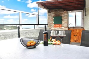 Ein Tisch mit einer Weinflasche, zwei Gläsern und einem Korb Orangen auf einer Terrasse mit Aussicht.