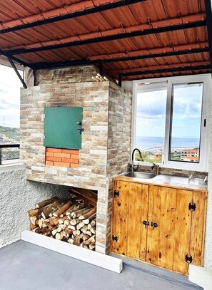 An outdoor kitchen with a stone and brick oven, a sink, and wooden cabinets. - Yara House by Stayguest (Câmara De Lobos)