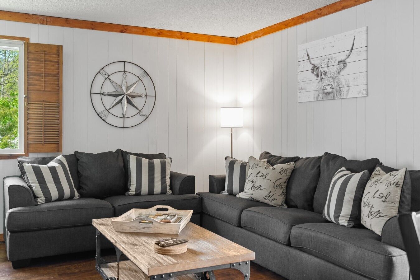 A living room with a sectional sofa, a wooden coffee table, a wall clock, and a lamp.