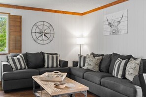 A living room with a sectional sofa, a wooden coffee table, a wall clock, and a lamp.