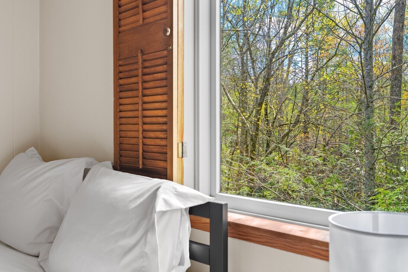 A bedroom with a bed, a window with a view of a forest, and a wooden door.