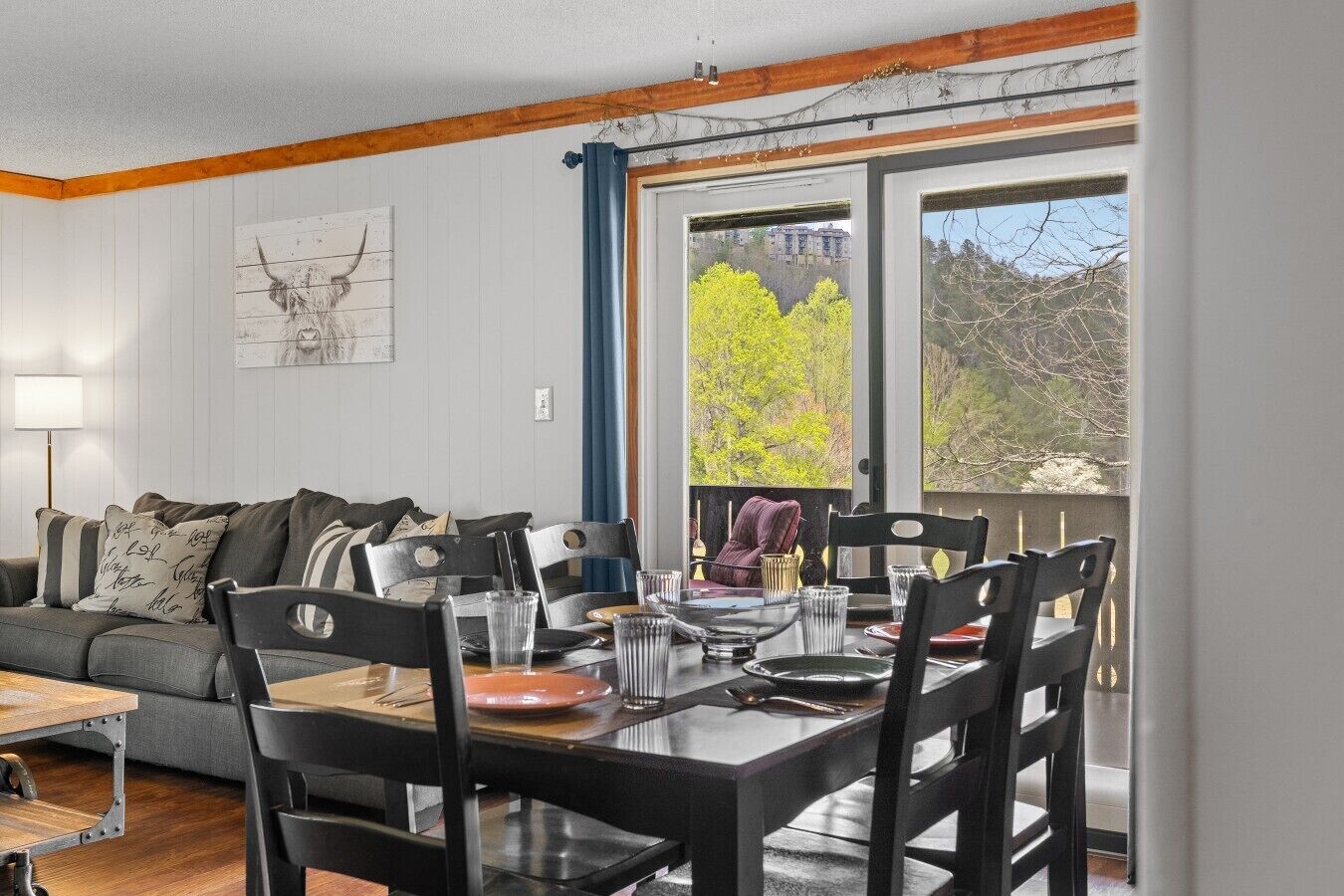 A dining area with a table set for four, a sofa, and a window with a view of trees and buildings.