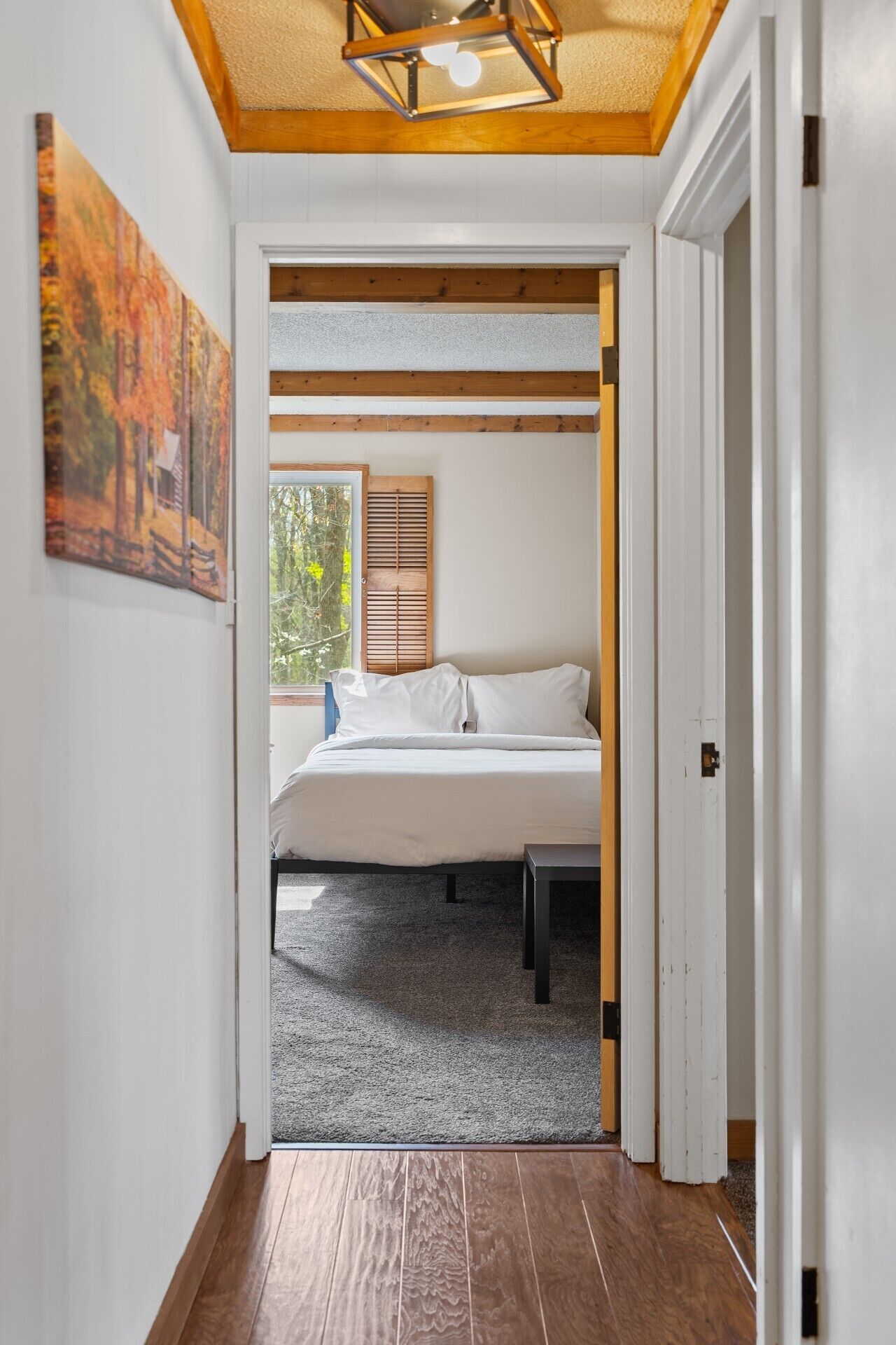 A bedroom with a bed, a window with blinds, and a painting on the wall.