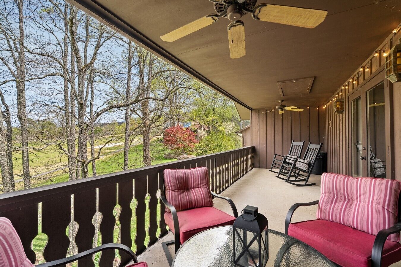 A covered outdoor area with a ceiling fan, a glass table, and seating with cushions.