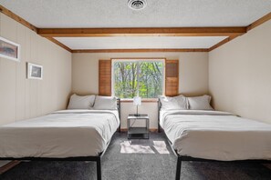 Ein Zimmer mit zwei Betten, einem Fenster mit Rollläden, einem kleinen Tisch und einem Deckenventilator.