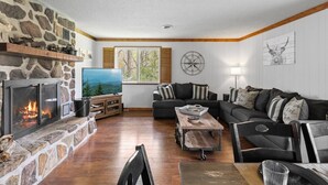 Ein gemütliches Wohnzimmer mit Kamin aus Stein, einem Fernseher, einem Holztisch und einer Couch mit gestreiften Kissen.