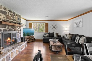 Ein gemütliches Wohnzimmer mit Kamin aus Stein, einem Fernseher, einem Holztisch und einer Couch mit gestreiften Kissen.
