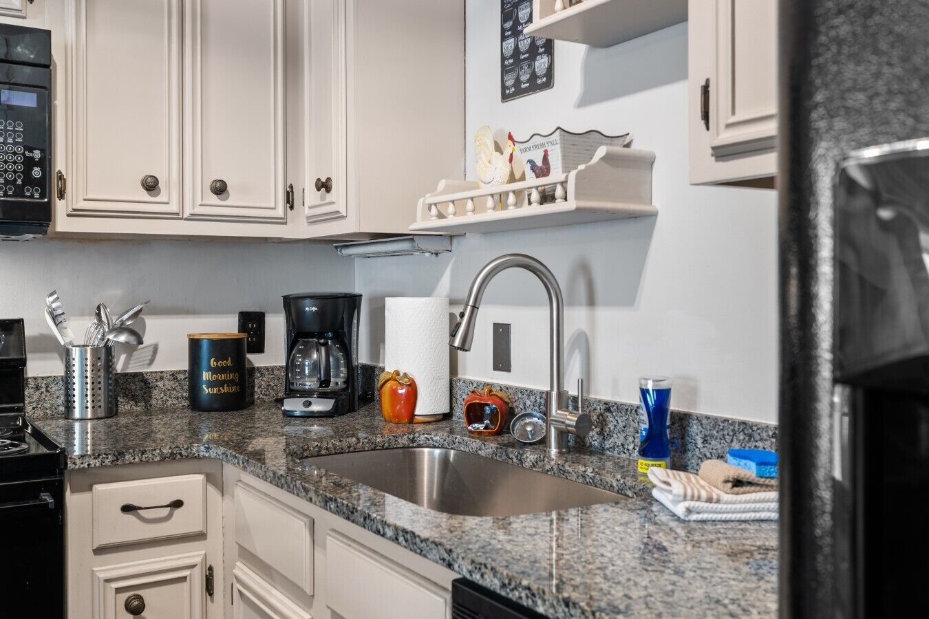 A kitchen with white cabinets, a stainless steel sink, a coffee maker, and various kitchen utensils.