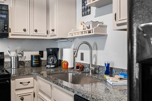 A kitchen with white cabinets, a stainless steel sink, a coffee maker, and various kitchen utensils. - Mountain View Loft | Cozy Single-Level Retreat (Gatlinburg)