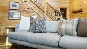 A modern living room with a grey sofa, two framed pictures on the wall, and a wooden staircase in the background. - Serene MTN Cabin: Indoor Pool, Hot Tub, & Game Room! (Pigeon Forge)