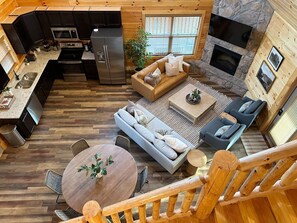 Interior de cabana com cozinha, área de refeições e espaço de estar, incluindo lareira.