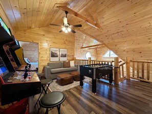 A cozy room with a wooden ceiling, a sofa, a foosball table, and a gaming console. - Serene MTN Cabin: Indoor Pool, Hot Tub, & Game Room! (Pigeon Forge)