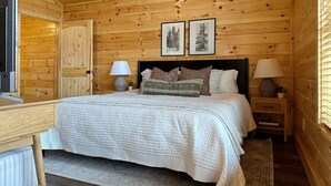 A wooden cabin bedroom with a bed, two bedside tables with lamps, a desk, and a window with blinds. - Serene MTN Cabin: Indoor Pool, Hot Tub, & Game Room! (Pigeon Forge)