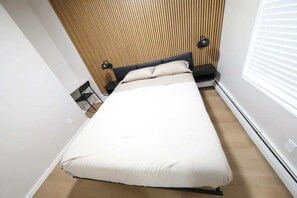 A bedroom with a bed, a nightstand, a lamp, and a window with blinds. - Modern apt in E Boston/Walk to Airport (Boston)