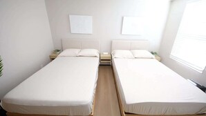 Una habitación con dos camas individuales, una mesita de noche con lámpara y una ventana con persianas.