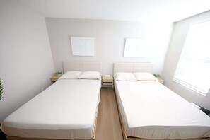 A room with two single beds, a bedside table with a lamp, and a window with blinds. - Modern apt in E Boston/Walk to Airport (Boston)