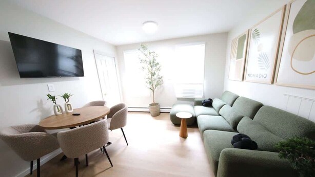 Una sala de estar moderna con una televisión de pantalla plana, una mesa redonda de madera con sillas, un sofá verde y una planta en maceta.