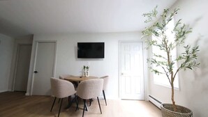 Un comedor con una mesa y sillas, un televisor en la pared y una planta en maceta.