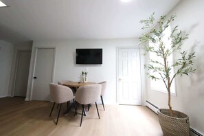 A dining area with a table and chairs, a television mounted on the wall, and a potted plant. - Modern apt in E Boston/Walk to Airport (Boston)