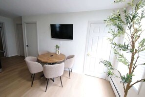 A dining area with a round table and four chairs, a flat-screen TV mounted on the wall, and a potted plant. - Modern apt in E Boston/Walk to Airport (Boston)