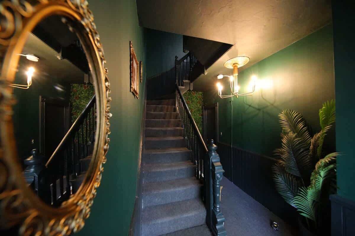 A staircase with a handrail, a wall-mounted mirror, and wall sconces.
