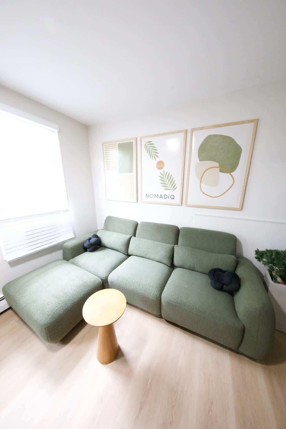 A modern living room with a sectional sofa, a round wooden side table, and framed artwork on the wall.