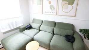 Una sala de estar moderna con un sofá modular, una mesita redonda de madera y cuadros en la pared.