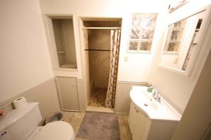 A bathroom with a toilet, sink, shower, and a small window.