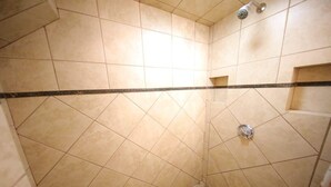 Un área de ducha con paredes y suelo de baldosas, un cabezal de ducha y desagüe.