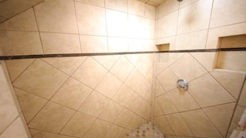 A shower area with tiled walls and floor, a showerhead, and a drain.