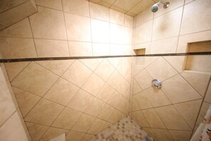 Un espace douche avec des murs et un sol carrelés, une pomme de douche et un drain.