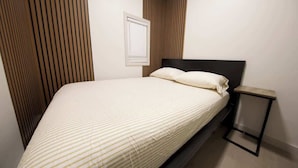 Un lit avec une tête de lit, une table de chevet et un luminaire fixé au mur.