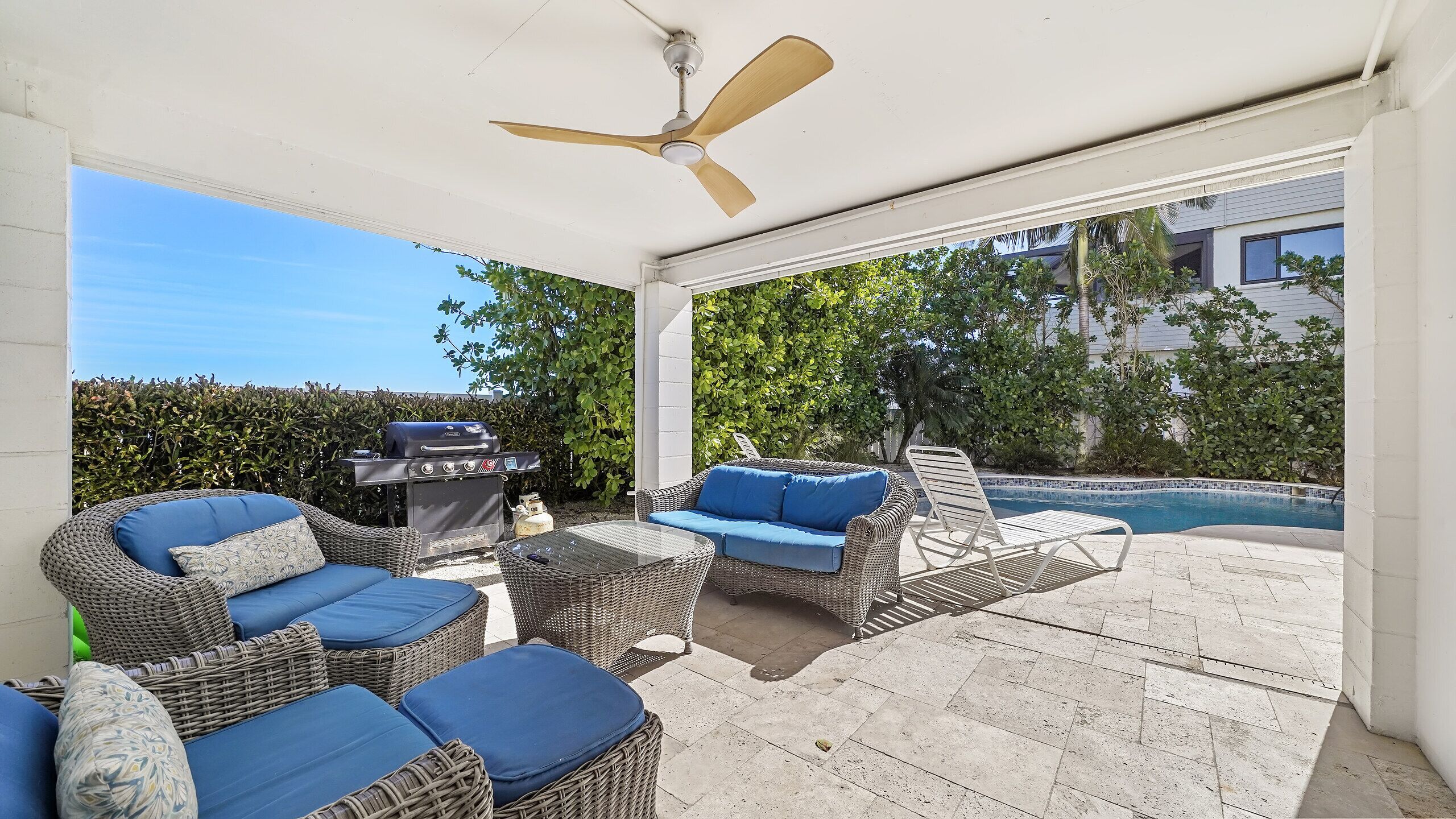 A covered outdoor seating area with wicker furniture and a pool in the background.