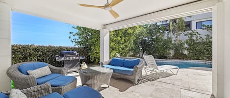 A covered outdoor seating area with wicker furniture and a pool in the background.