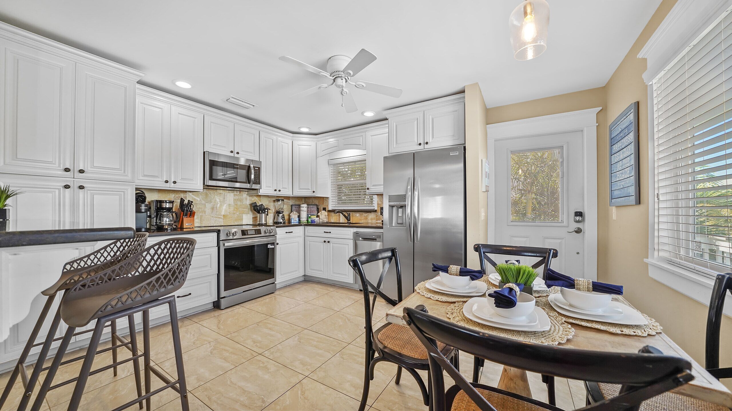 A modern kitchen with white cabinetry, a stainless steel refrigerator, and a dining area with a table set for two.