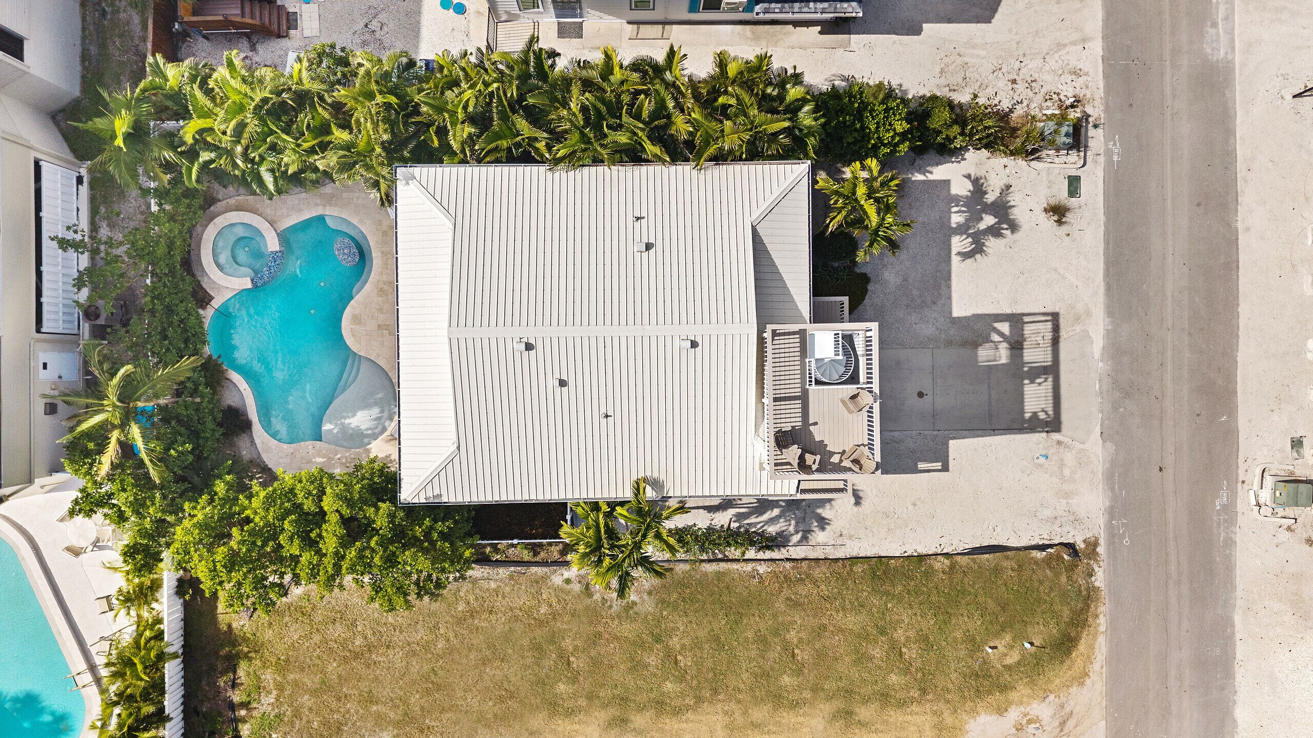 An aerial view of a property with a swimming pool, a covered patio area, and surrounding greenery.