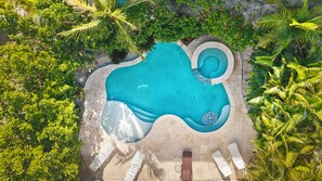 Vista aérea de una piscina de forma singular rodeada de abundante vegetación y algunas sillas de descanso.