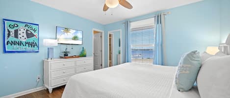 Un dormitorio con cama, ventilador de techo, televisor y ventana con vista.