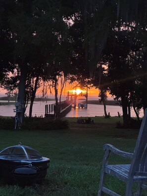 Solnedgang over et sølandskab med en anløbsbro og en pavillon.