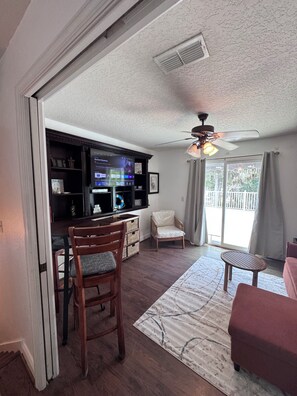 A living room with a television, a ceiling fan, a dining area, and a view of the outdoors. - COZY LAKE FRONT 1-bedroom apartment, kitchen, balcony on East Lake TOHO. (St. Cloud)