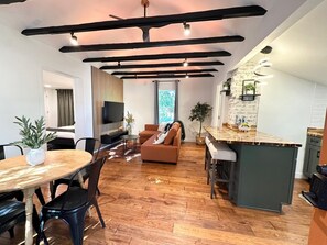 Ein modernes Wohnzimmer mit Holzboden, einer Couch, einem Fernseher und einem Essbereich mit Tisch und Stühlen.